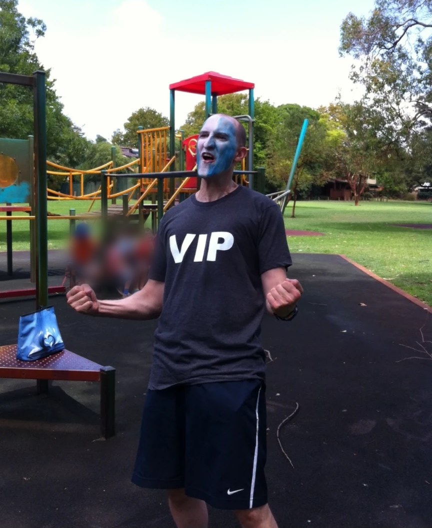 Andrew Wallis in blue and white Braveheart face paint and a VIP T-shirt, fists clenched, in a park playground